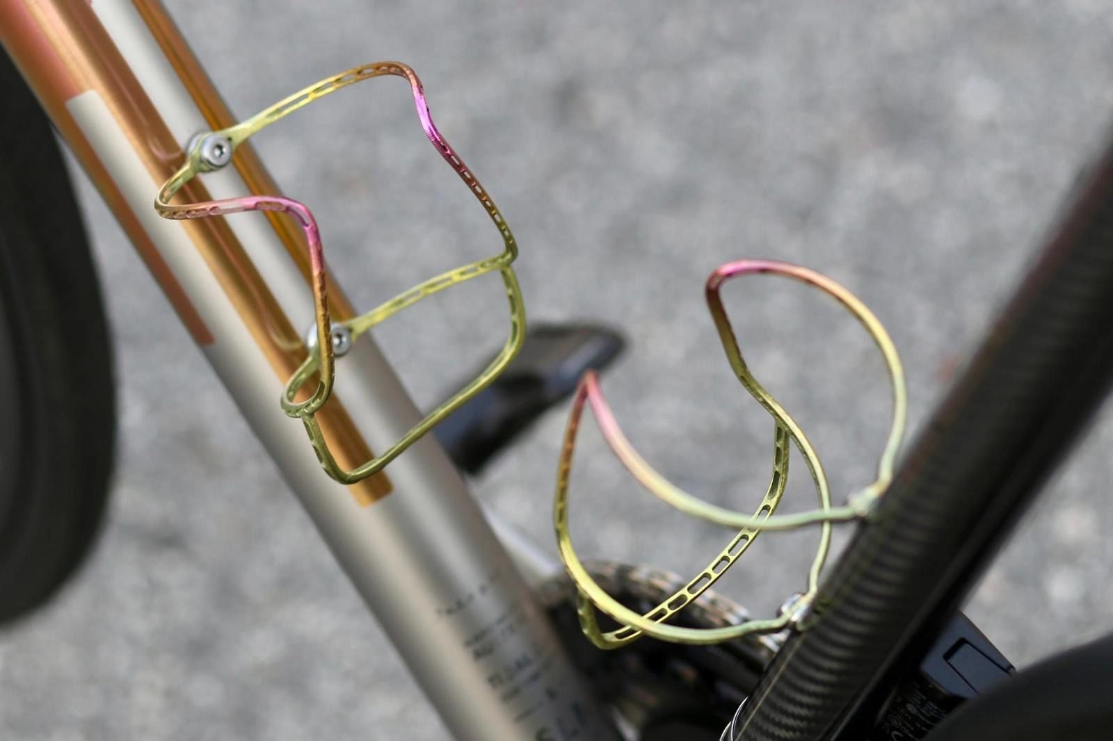 Close-up of two anodized titanium bottle cages mounted on a bicycle frame