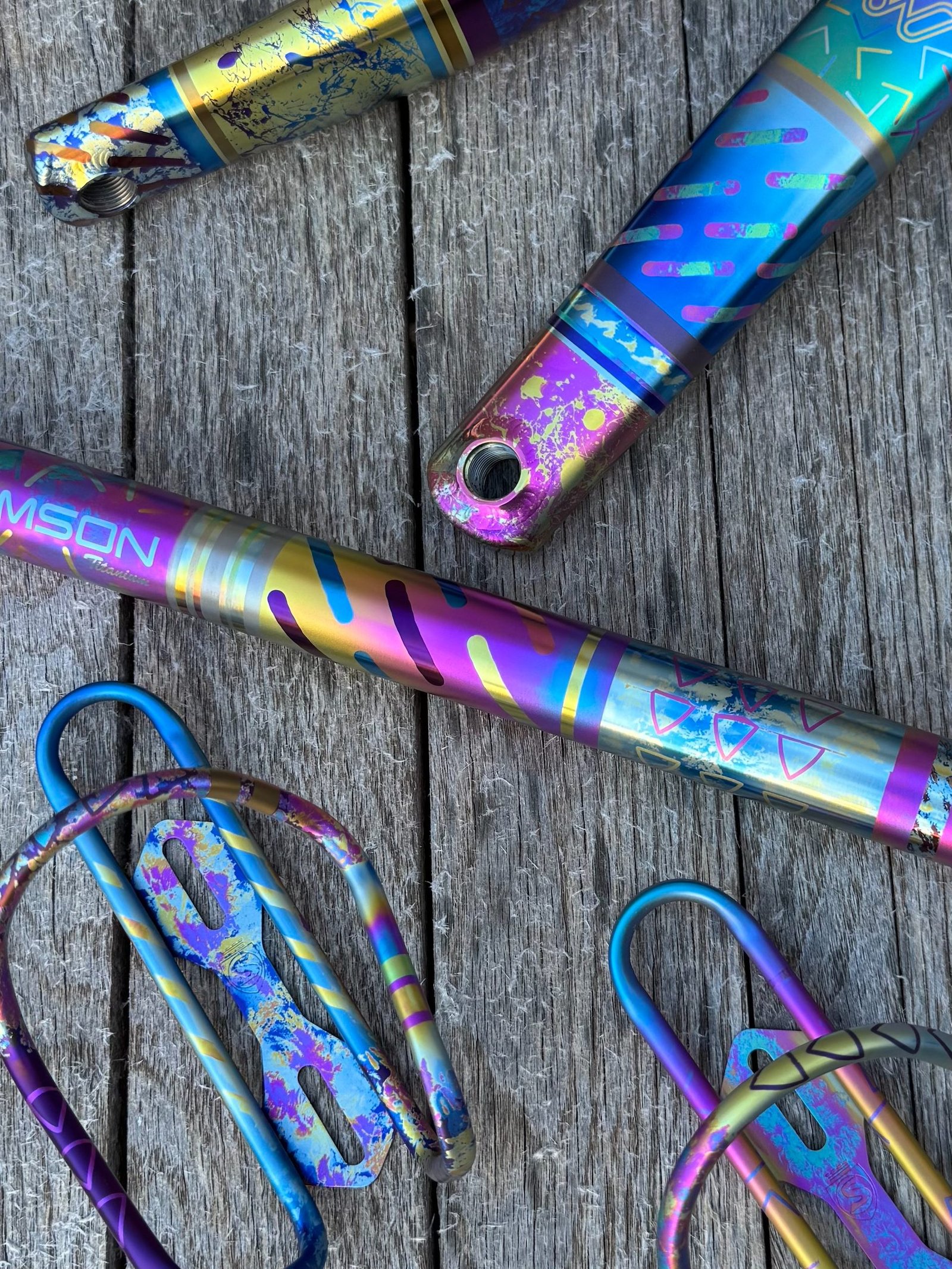 Brightly anodized titanium tubes and bottle cages arranged on weathered wood